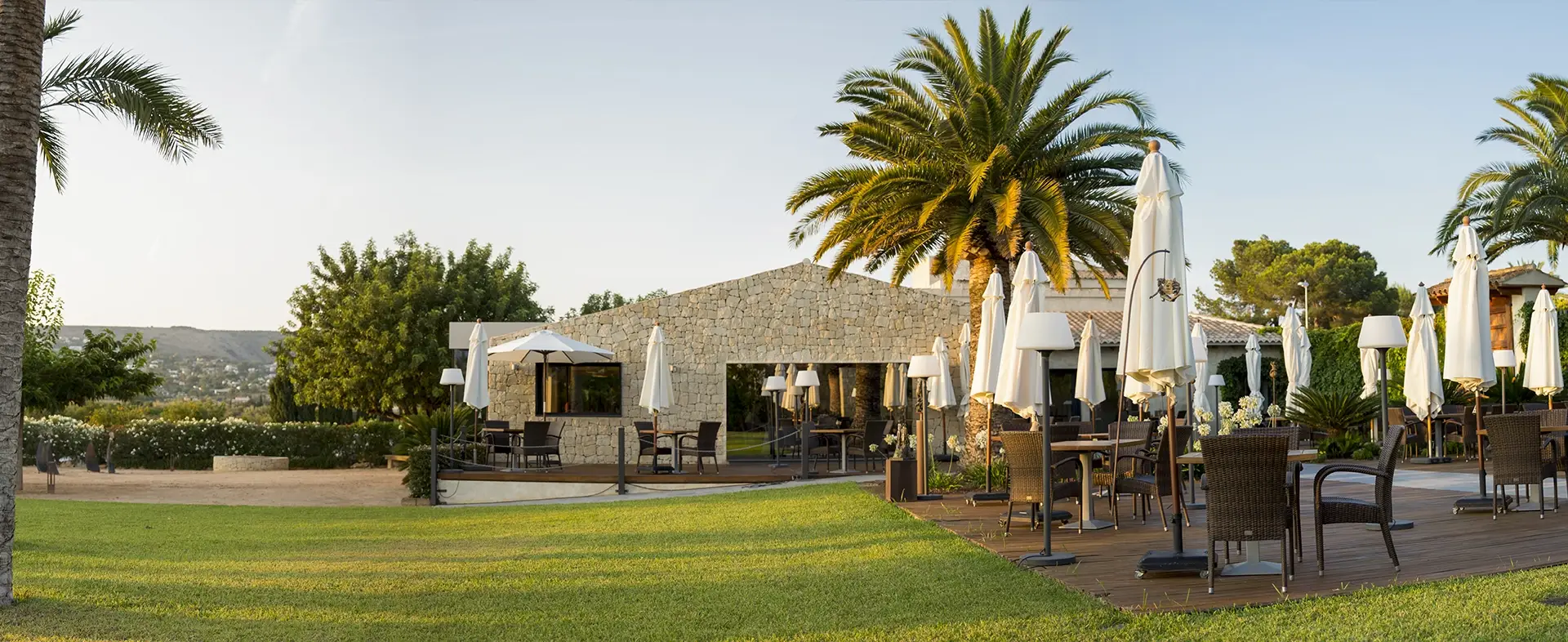 Elegant outdoor dining terrace at the Michelin-starred BonAmb Restaurant in Javea, with tables set on a lawn under white parasols, surrounded by palm trees.