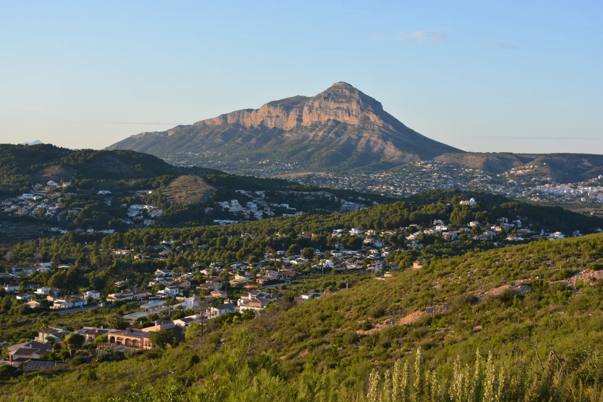Panoramic view of the Montgó mountain massif on the Costa Blanca, Spain, with residential areas nestled at its base and verdant hills in the foreground.