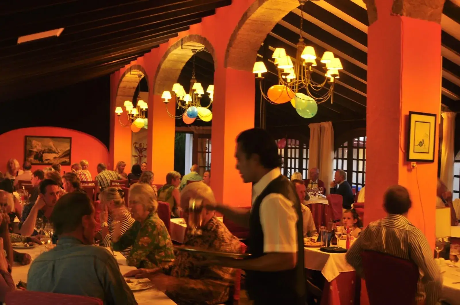 Lively restaurant interior at night featuring diners, arched architecture, and warm lighting